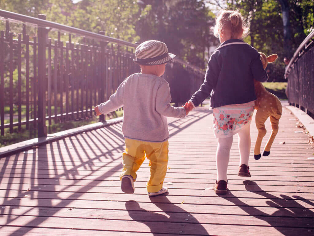 Es parte de su desarrollo que los niños pequeños se orinen en los pantalones. Niños atravesando un puente peatonal en un parque. Uno de ellos va orinado.