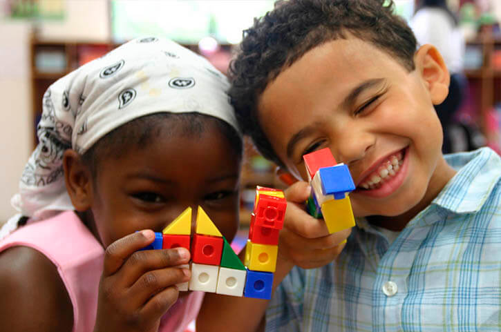 Una niña y un niños, con unos blocks didácticos, mirando a cámara sonrientes.