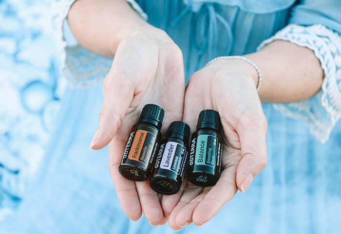 Manos de mujer sosteniendo tres botellitas de 15 ml de aceites esenciales de incienso, lavanda y Balance, la mezcla del bienestar.